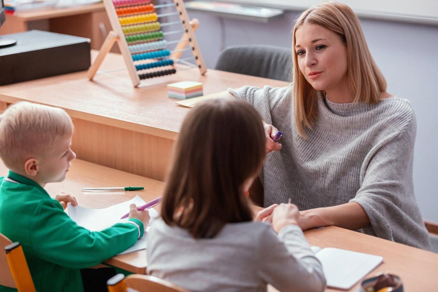 Teacher giving one-on-one support to two children at a desk in a modern Ajman school