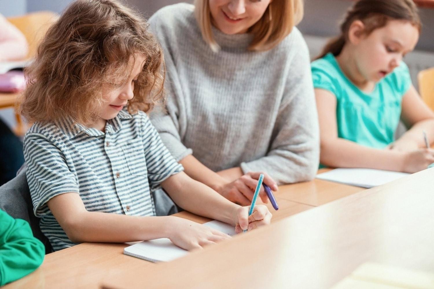 Teacher helping a boy with his writing while classmates work independently